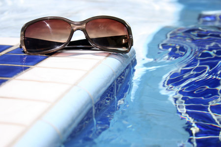 Sunglasses by bright swimming pool with mosaic pattern