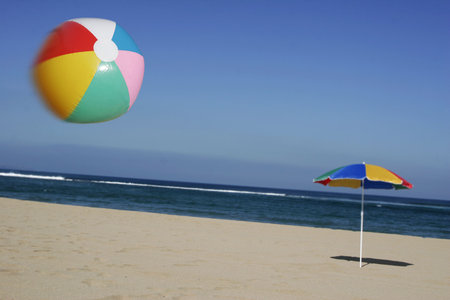 Brightly colored beachball in the air with beach and parasol behindの写真素材