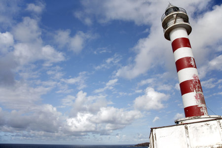 Old red and white lighthouse on clifftop with blue skyの写真素材