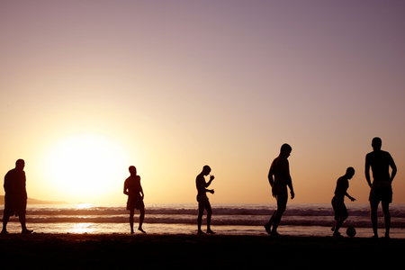 A game of football on the beach at sunsetの写真素材