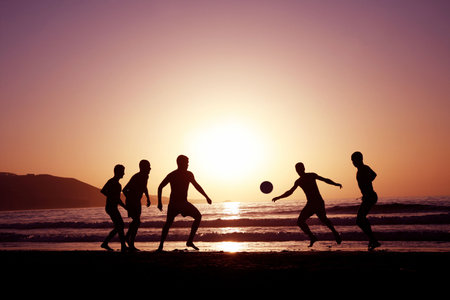 A game of football on the beach at sunsetの写真素材