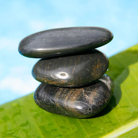 Square formatt photo of pebble stack with banana leaf and blue water
