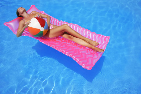 Woman floating in pool with beachballの写真素材