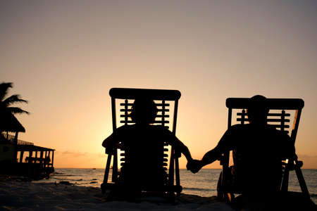 Couple in deckchairs holding hands at sunsetの写真素材