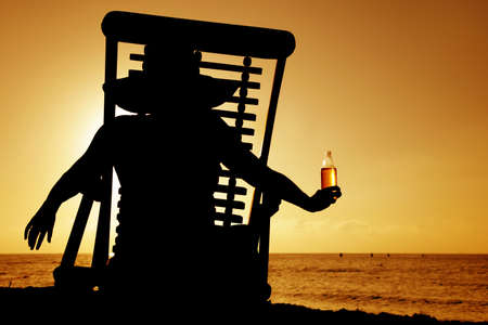 Woman drinking beer in a deckchair at sunsetの写真素材