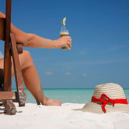 Woman sitting in a deckchair drinking beer with a hat in the foregroundの写真素材