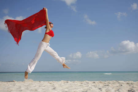 Woman jumping on the beach with red sarongの写真素材