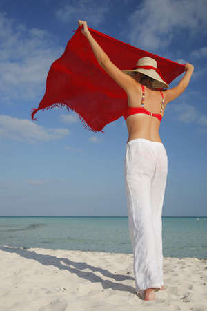 Woman shaking out a saong on a tropical beachの写真素材