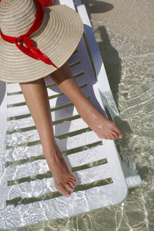 Pretty woman sitting on a lounger with her feet in gorgeous waterの写真素材