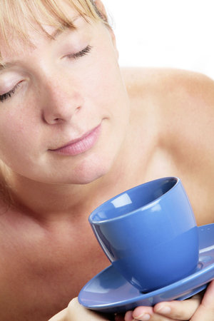 Woman in soft light drinking coffee from a blue cup and saucerの写真素材