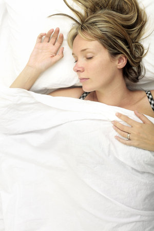 Woman asleep in a bed with white sheetsの写真素材