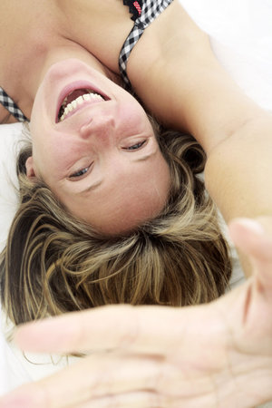 Woman in bed smiling with her hand held up to the cameraの写真素材