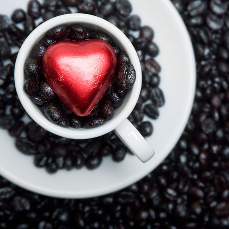 White coffee cup and saucer with roasted beans and red candy heartの写真素材