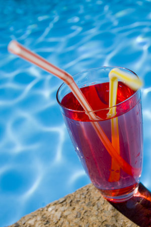 Wide angle shot of a red cocktail by the side of a blue swimming pool