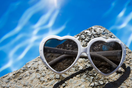 Heart-shaped sunglasses by a blue poolの写真素材