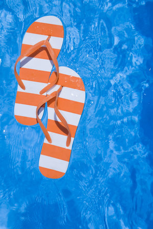 Pretty pair of stripey flip flops or thongs in a sparkling blue swimming poolの写真素材