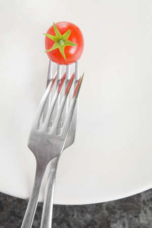 Two interlinked forks on a white plate with a tiny cherry tomato