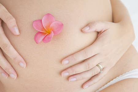 Close up of pregnant woman holding her tummy with a flower in her belly button.の写真素材