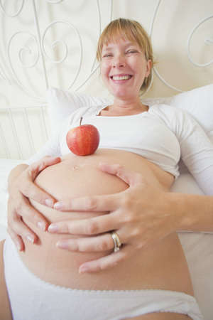 Smiling pregnant woman in high key with an apple on her bellyの写真素材