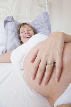 Pregnant woman smiling in bed. Focus is on the belly and hand.の写真素材