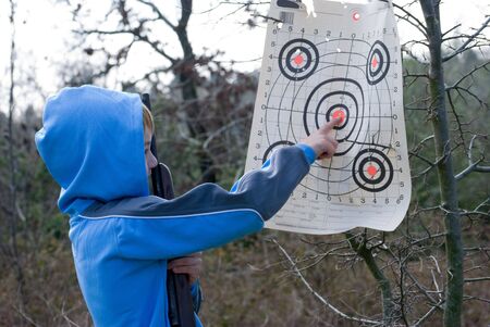 Young boy pointing out bullseye shot while holding rifleの写真素材