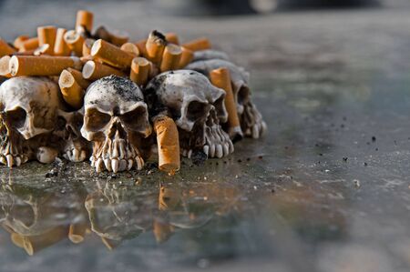 Ashtray of skulls filled with cigarette butts and ashesの写真素材