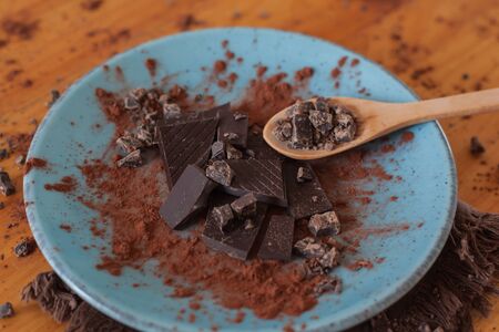 Ounces of healthy chocolate with pure cocoa on a blue plate with a wooden spoon with cocoa and a...
