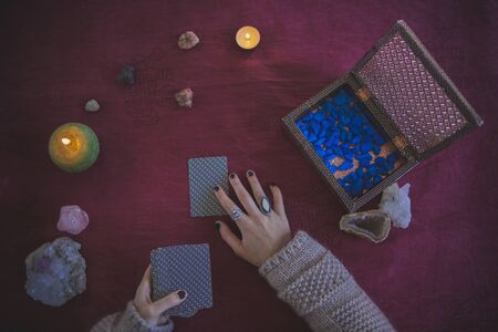 Young woman placing a tarot card to predict the future, with a mystical background of candles,...