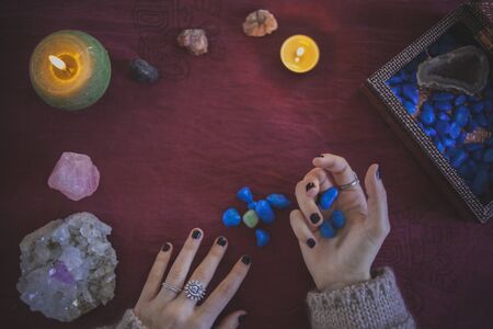 Young woman catching and observing precious stones with a mystical background of crystals and candlesの写真素材