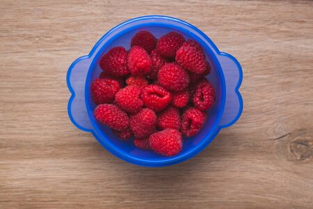 Phantom blue bowl full of raspberries with a rustic wooden backgroundの写真素材