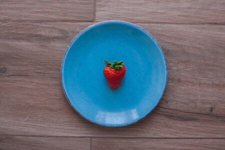 Strawberry on a blue plate with rustic wooden background