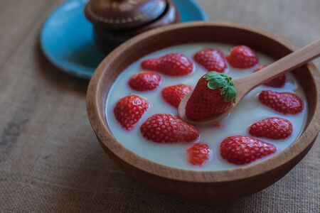 Strawberries with oat milk on a wooden bowl with a wooden spoon and another in the background on a blue plateの写真素材