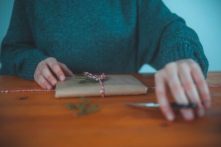 Young woman picking up scissors while wrapping Christmas presents with rustic background