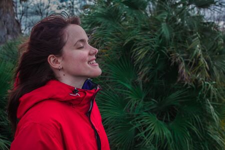 Young woman with red pea coat in the field relaxing while winding and smilingの写真素材