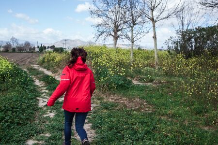 Young woman with red pea coat in the field runningの写真素材
