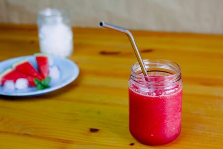 Closeup of a watermelon slush, pieces of watermelon with ice and peppermint on a blue plate and a glass jar with crushed ice in the backgroundの写真素材