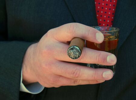 man in suit smoking a cigar and holding a shot of whiskeyの写真素材