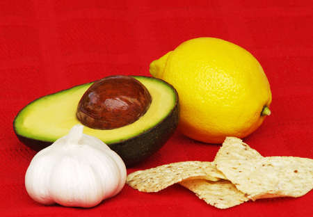 an avocado half, garlic, lemon and tortilla chips on red clothの写真素材