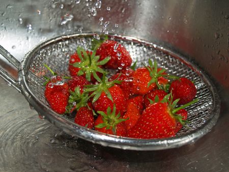 red strawberries being rinsed in the sink