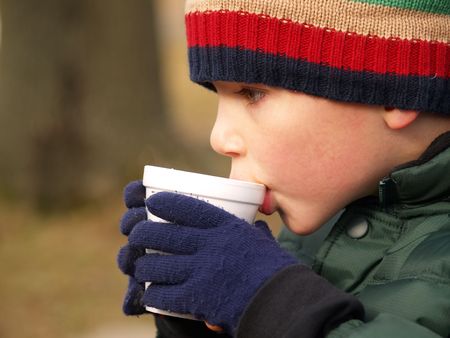 young boy with hat and gloves drinking hot chocolate outdoorsの写真素材
