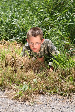 young boy in cammoflage crawling out of the grass の写真素材