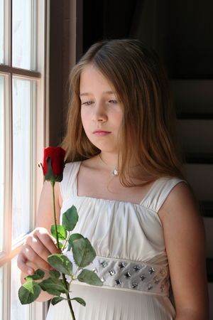 pretty young girl holding a red rose next to a windowの写真素材