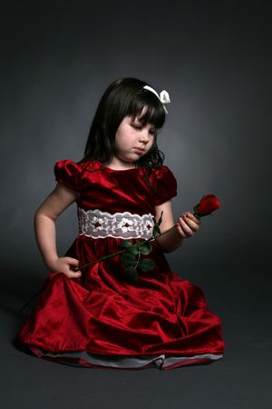 cute girl in red holiday dress looking at flowerの写真素材