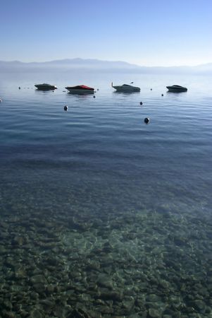 Four boats on the water with clear shallow water in the forground and mountains in the background.の写真素材