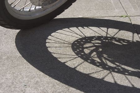 The wheel of a motorcycle casts a shadow on the sidewalk.の写真素材