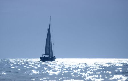 A sailboat cruises in the sparkling waters of sunset.の写真素材