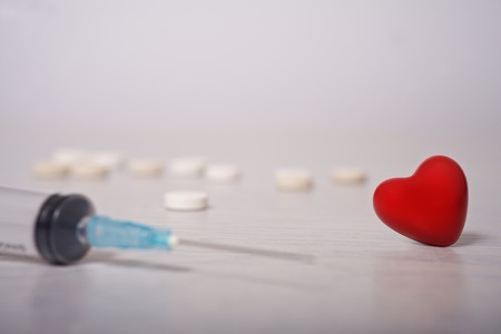 Syringe and pills laid out in the form of heart on a white background.の写真素材