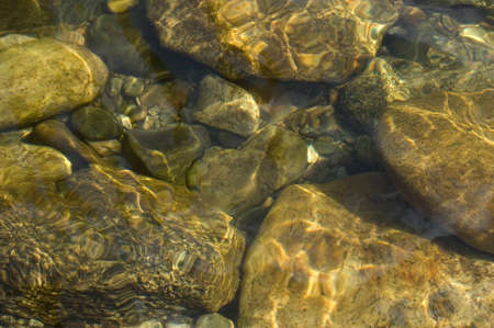 River rocks underwater with sun reflecting off the movement of the water.の写真素材