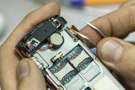 Elderly and young men repair a mobile phone together. They work in a repair shop. They use different tools. They are repair specialists.の写真素材