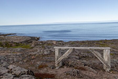 View of a deserted beach on a sunny morning - a painted bench next to the surf line against the...